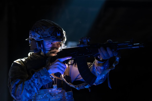 Soldado del ejército con uniformes de combate con un rifle de asalto y un casco de combate en una misión nocturna de fondo oscuro. Efecto de luz de gel azul y morado. Foto de alta calidad