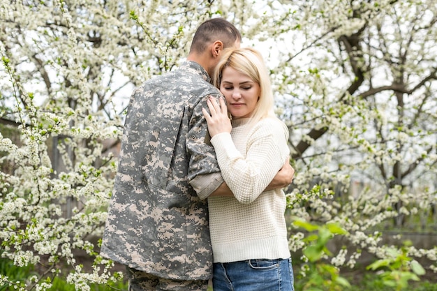 El soldado está abrazando a una mujer al aire libre. Reunión de una pareja en el parque de la tarde.