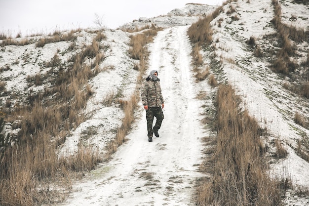 El soldado está de pie con el uniforme de camuflaje y el pañuelo keffiyeh shemagh a cuadros. El hombre está al aire libre en el lugar desierto abandonado.