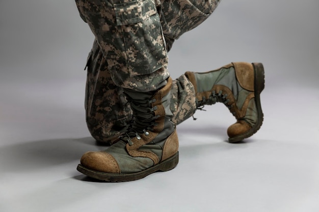 El soldado está sobre una rodilla. Piernas con uniformes de camuflaje y botas del ejército estadounidense. Memorial Day y conflictos militares. De cerca. Fondo gris.