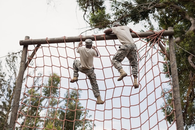 Soldado militar escalando uma rede durante uma pista de obstáculos no campo de treinamento