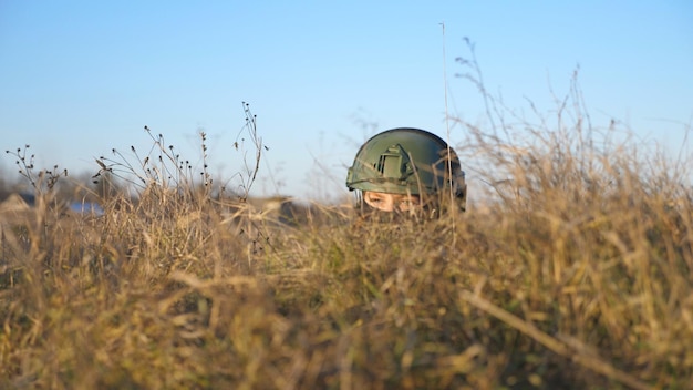 Soldado militar en traje y casco escondido en una trinchera durante el bombardeo y viendo al ejército enemigo Soldado ucraniano mirando desde el refugio escondido detrás de una colina del ataque Guerra en Ucrania