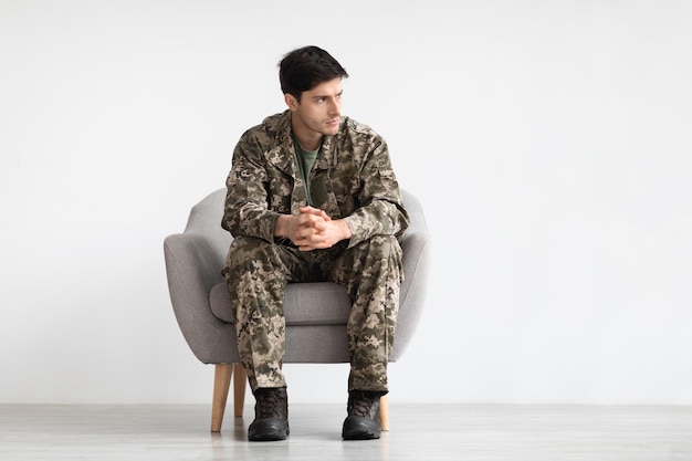 Soldado molesto sentado en un sillón sobre fondo blanco.