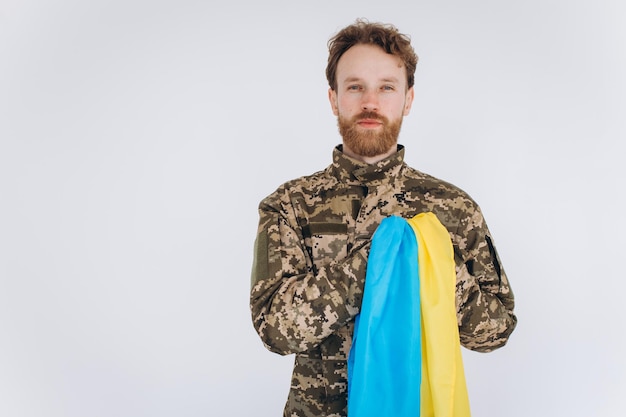 Soldado patriota ucraniano em uniforme militar segura a mão em um coração com uma bandeira amarela e azul sobre fundo branco