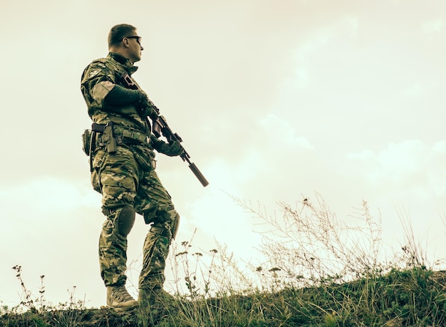 Soldado con rifle de pie en el campo contra un cielo despejado