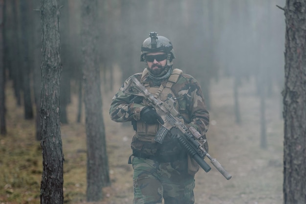 Soldado totalmente equipado em um uniforme de camuflagem emergindo de uma nuvem de fumaça no meio de um pinheiro