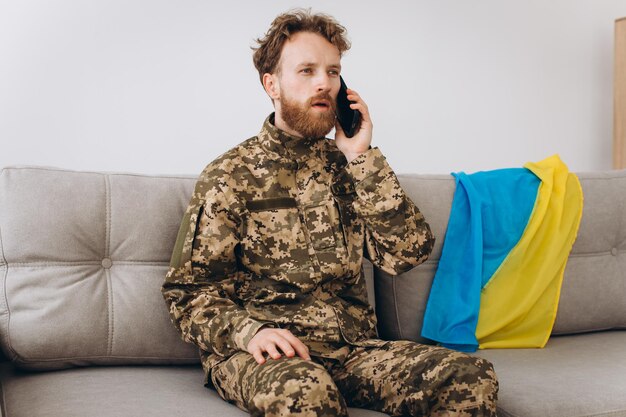 Un soldado ucraniano con uniforme militar está sentado en un sofá en la oficina y hablando por teléfono