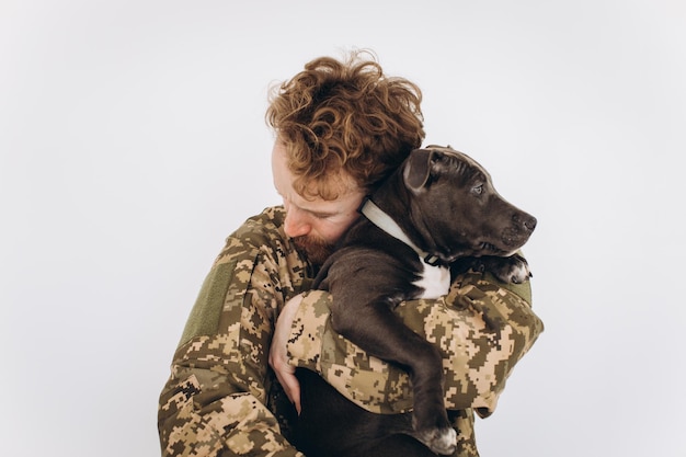 Soldado ucraniano con uniforme militar sostiene a un perro en sus brazos con un fondo blanco