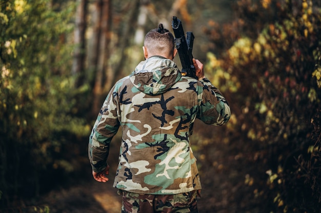 Soldado en uniforme de camuflaje con un rifle en el hombro caminar en el bosque.