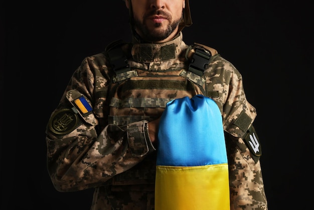 Soldado en uniforme militar con bandera ucraniana en primer plano de fondo negro