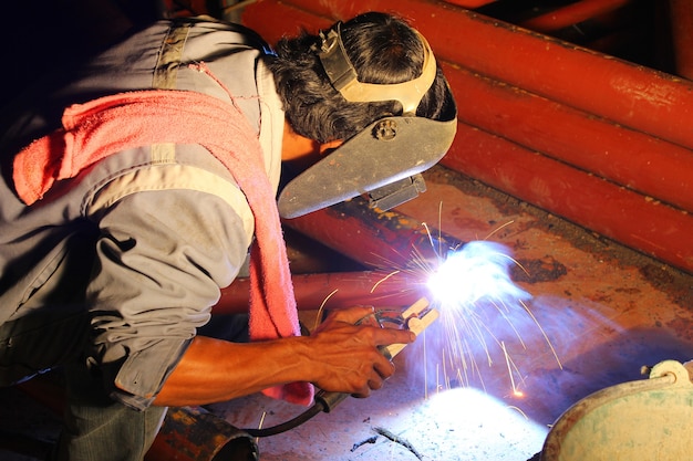 Soldador com máscara de proteção, solda de metal e faíscas de trabalho.