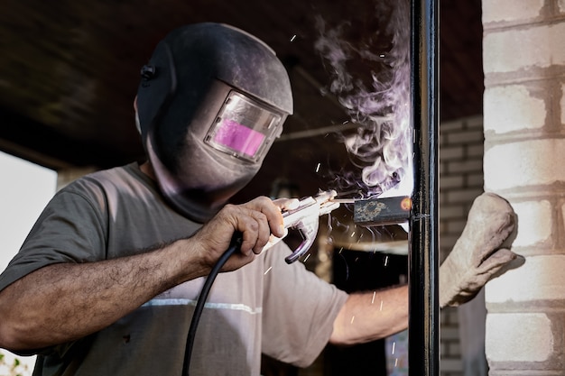 Foto soldador com máscara protetora de soldagem de metal realiza trabalho de soldagem