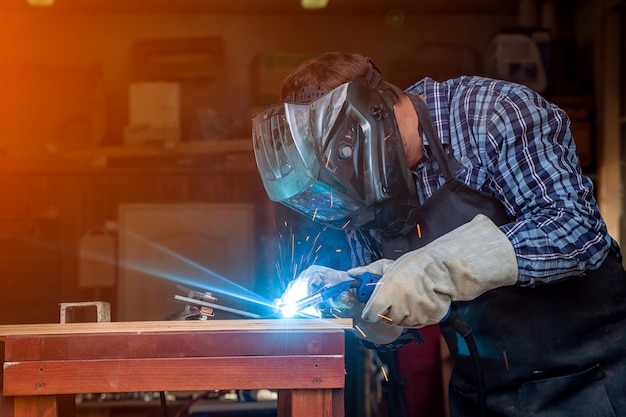 Foto soldador homem forte em roupas de trabalho, trabalhando duro e solda com uma máquina de solda de metal