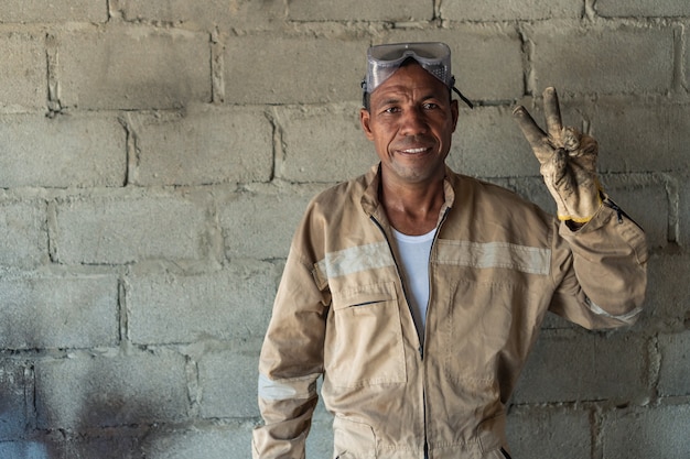 Soldador latino de pie en su lugar de trabajo sonriendo y mirando a la cámara