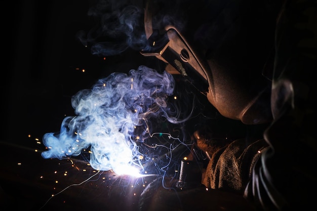 Soldador no trabalho Homem com máscara protetora O soldador faz costuras no metal