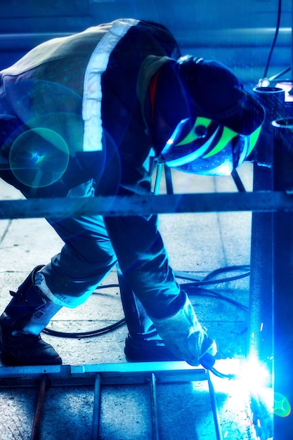 Foto soldador profissional em uniforme de proteção e máscara trabalha na sala de produção fluxo de trabalho autêntico