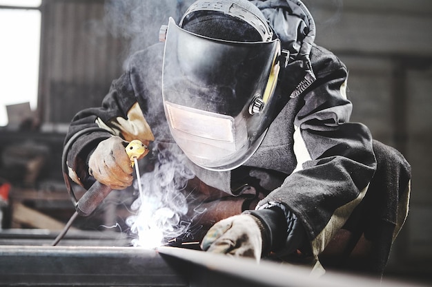 Soldador que trabaja con soldadura en estructuras metálicas en una planta industrial