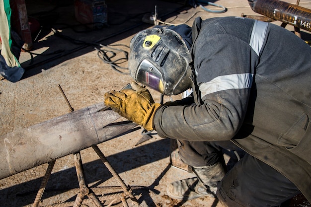 Soldador en ropa protectora para soldar. Preparación de tuberías para una plataforma de perforación. En el sitio de construcción.