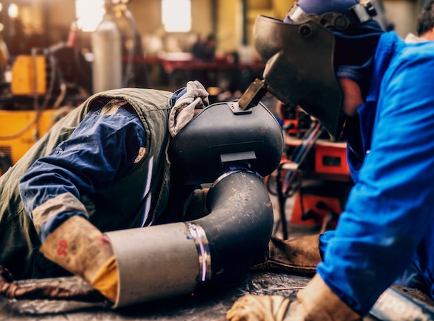 Soldadores profesionales en uniforme de protección y máscara de soldadura de tubos metálicos en el taller.