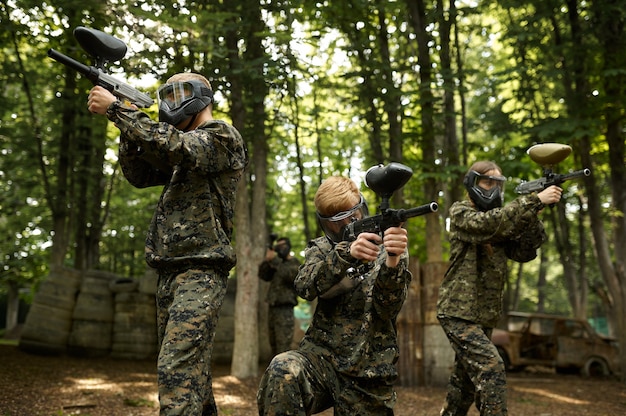 Soldados en camuflaje y máscaras jugando paintball en el bosque. Deporte extremo con arma neumática y balas de pintura o marcadores, juego de equipo militar al aire libre, tácticas de combate