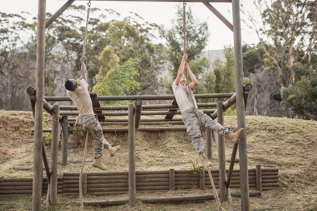 Soldados militares escalando corda durante o treinamento da pista de obstáculos no campo de treinamento