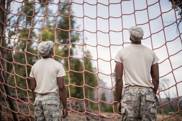 Soldados militares mirando net durante la carrera de obstáculos en el campo de entrenamiento