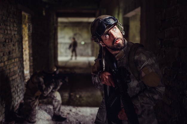 soldados de pie en el oscuro corredor del edificio vacío. Chico barbudo está mirando hacia arriba y sosteniendo el rifle.