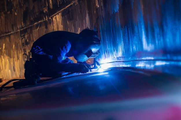 Foto soldagem arco argônio trabalhador masculino metal reparado está soldando faíscas tanque de construção industrial de óleo inoxidável dentro de espaços confinados.