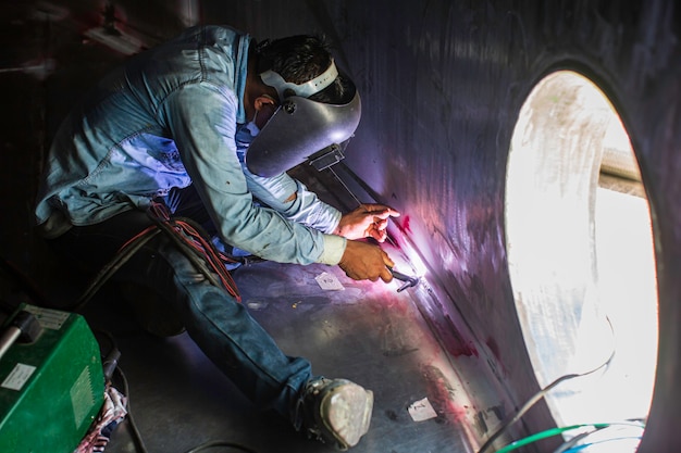 Soldagem de arco de argônio trabalhador masculino metal reparado está soldando faíscas óleo de tanque de construção industrial dentro de espaços confinados.