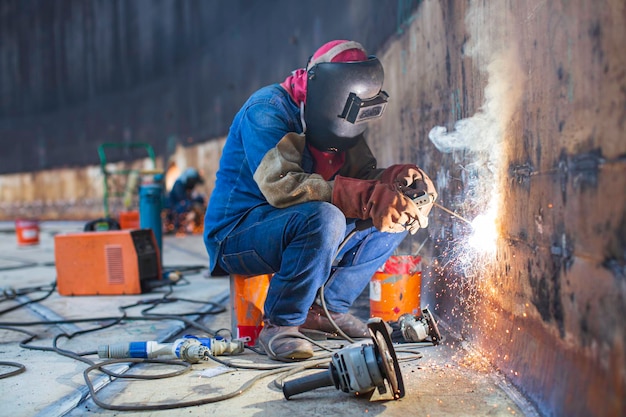 Foto soldar metal de trabajador masculino es parte de la construcción de la placa de la carcasa de la pared del tanque de maquinaria tanque de almacenamiento de petróleo y gas dentro de espacios confinados.