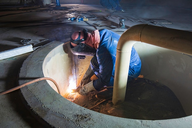 Soldar o metal do trabalhador masculino faz parte do tanque de armazenamento de óleo do reservatório do fundo da placa do tanque de máquinas dentro de espaços confinados.