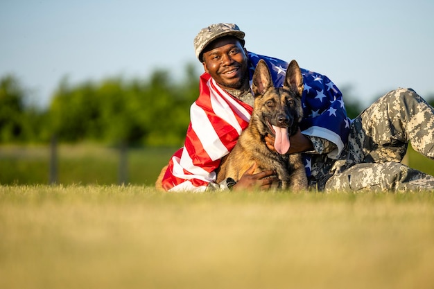 Soldat in Tarnuniform mit seinem Militärhund, der die US-Flagge hält und den Unabhängigkeitstag feiert