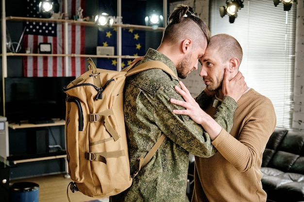 Foto soldat in uniform, der seinen freund umarmt und verspricht, nach militärübungen zurückzukehren