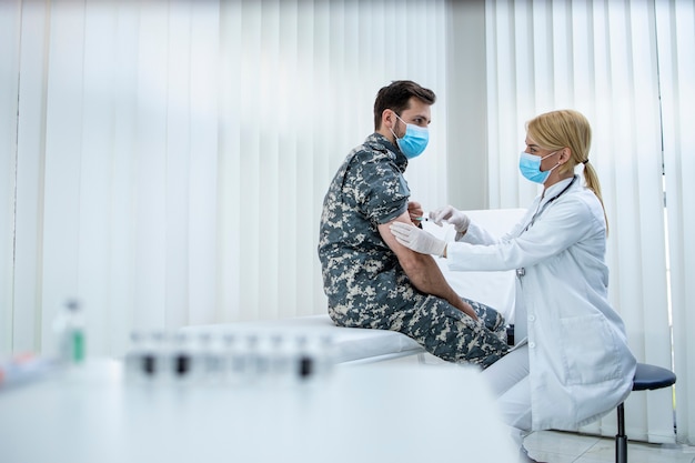 Soldat in Uniform erhält Impfstoff gegen Koronavirus in der Klinik