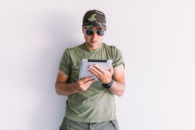 Soldat mit Sonnenbrille mit einem Tablet an einer weißen Wand