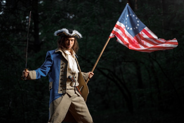 Soldat Patriot Rebell während des Unabhängigkeitskrieges der Vereinigten Staaten mit Flagge, die sich darauf vorbereitet, mit Säbel anzugreifen