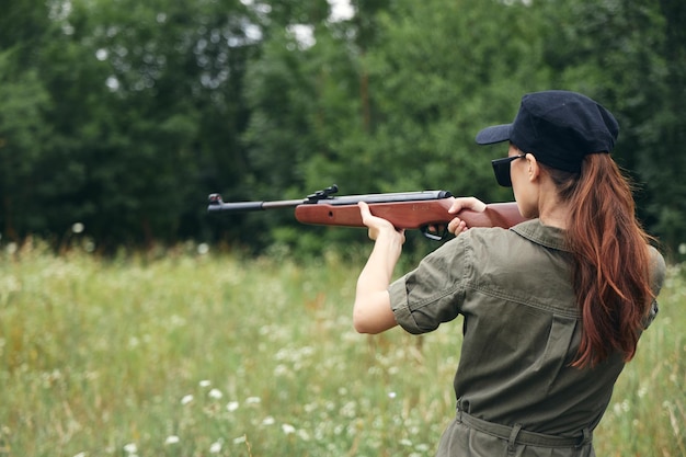 Foto soldatin rückansicht einer frau auf der jagd mit einer schrotflinte, sonnenbrille, schwarzer mütze