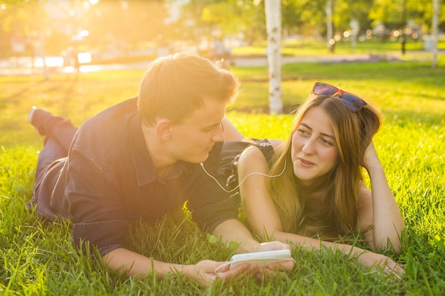 Soleado retrato de dulce pareja joven tumbado relajándose en la hierba juntos escucha música