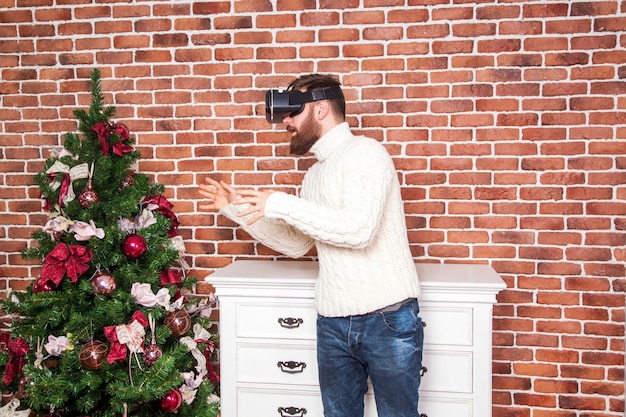 Soledad e ilusión de año nuevo. el retrato de hombre barbudo con gafas de realidad virtual cerca del árbol de año nuevo.