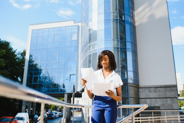 Solicitante de empleo afroamericano manteniendo una carpeta con CV en sus manos de pie contra el edificio de oficinas