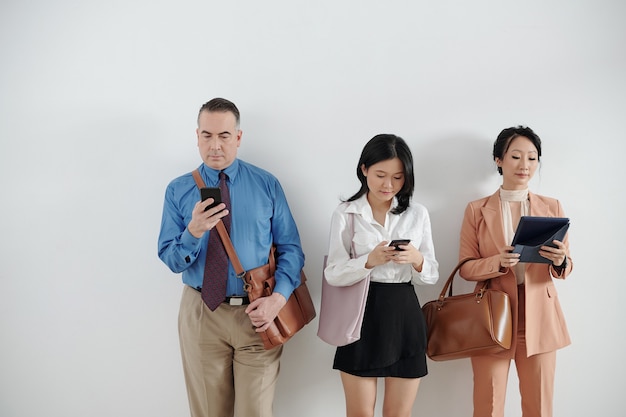 Solicitantes haciendo cola, esperando una entrevista de trabajo y revisando las redes sociales en teléfonos inteligentes y tabletas.