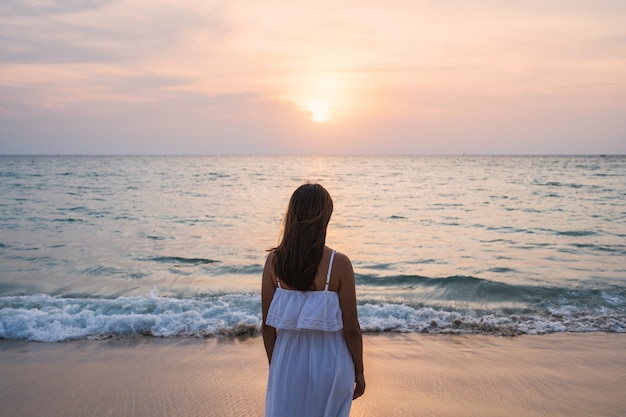 Solitária jovem mulher asiática em pé na praia ao pôr do sol