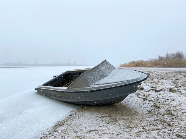 Un solitario barco de pesca a motor está estacionado bajo la nieve en el estacionamiento de invierno de la orilla del río