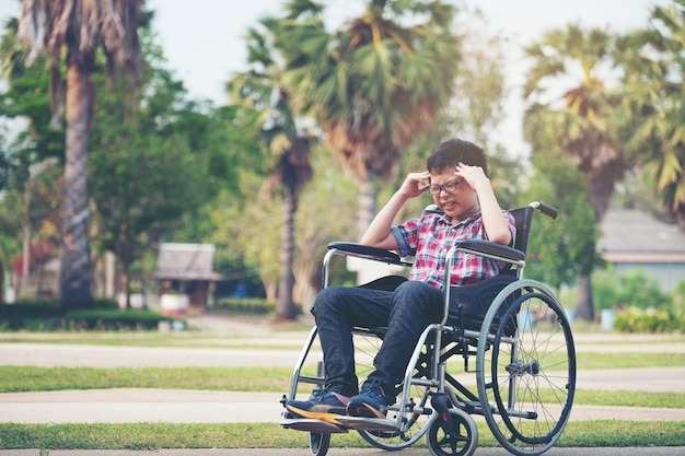 Solo asia boy en silla de ruedas con dolor de cabeza en el parque