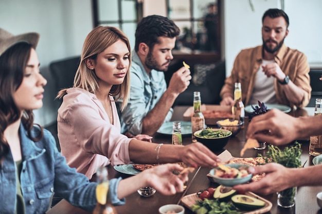 Solo hambriento. Grupo de jóvenes en ropa casual comiendo mientras tiene una cena en el interior