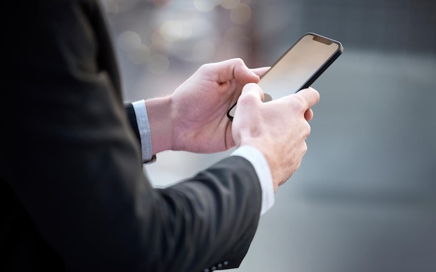 Solo un hombre de negocios moderno haciendo negocios modernos. Captura recortada de un hombre de negocios irreconocible parado en la ciudad y usando su celular.