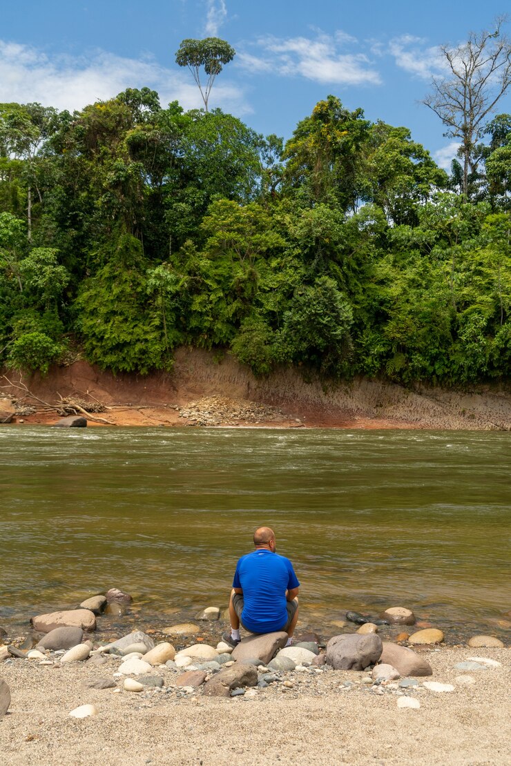 Foto un solo hombre sentado a la orilla del río en la selva amazónica, ecuador,