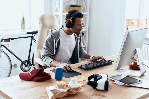 Solo jugando en casa. Hombre joven concentrado en ropa casual usando la computadora mientras pasa tiempo en casa