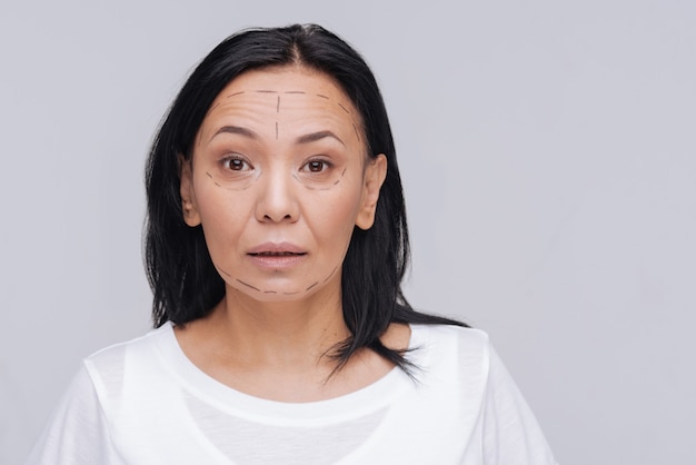 Solo un pequeño toque. Agradable joven asiática con pautas de cirugía especial en su rostro y de pie