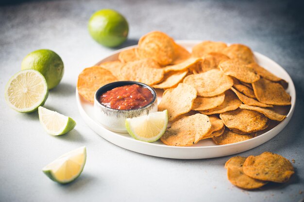 Un solo plato blanco grande de chips de nachos de tortilla de maíz amarillo con salsa de salsa sobre una mesa blanca